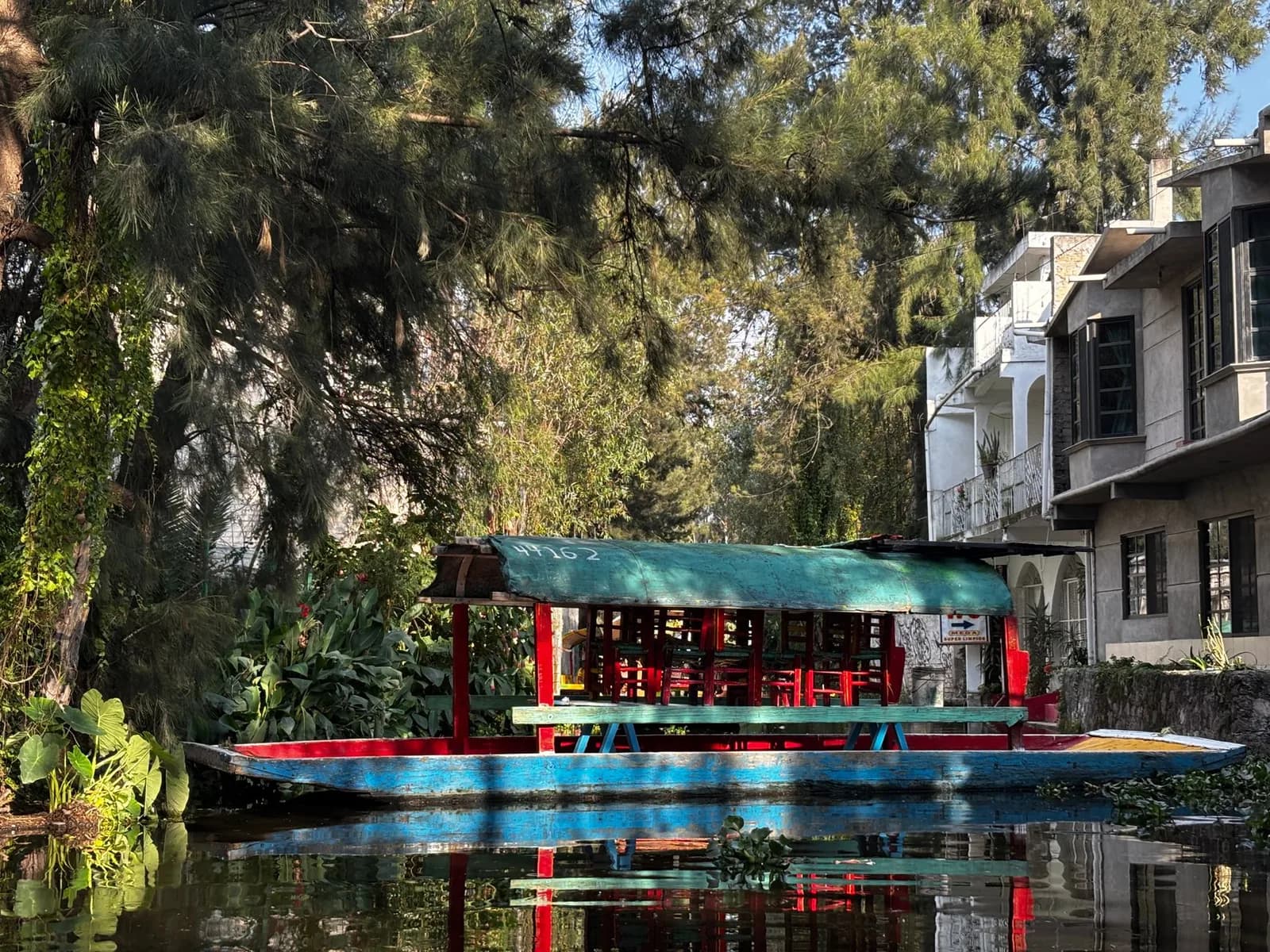 Trajinera aux toits verts et rouges sur un canal bordé d'arbres et de maisons à Xochimilco, au sud de Mexico
