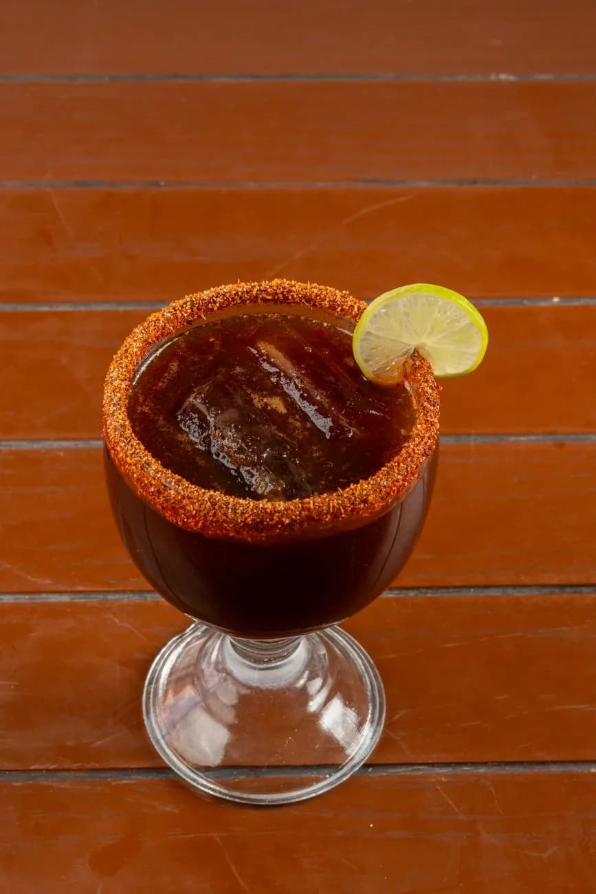 Michelada mexicaine servie dans un verre au bord givré de piment, avec une rondelle de citron vert