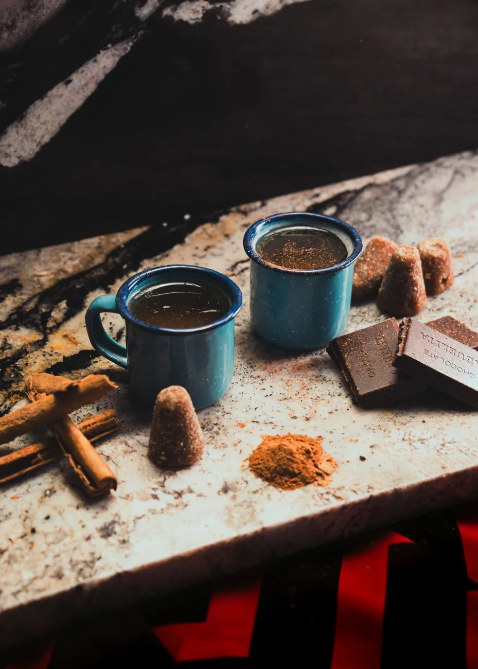 Chocolat chaud mexicain servi dans deux tasses émaillées, avec bâtons de cannelle, piloncillo et tablettes de chocolat