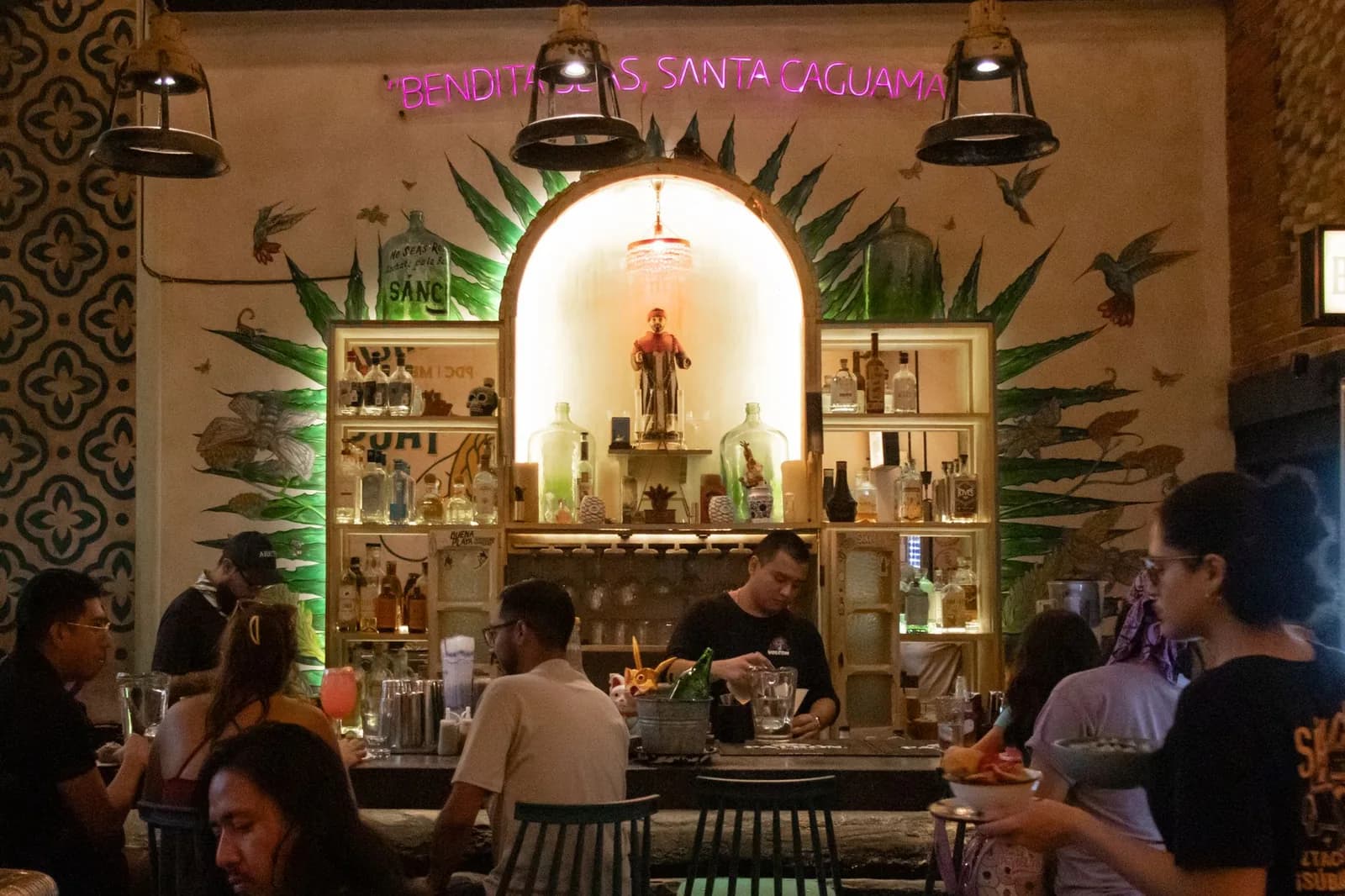 Ambiance animée d'une cantina mezcalería à Mexico, clients au comptoir sous une fresque d'agave