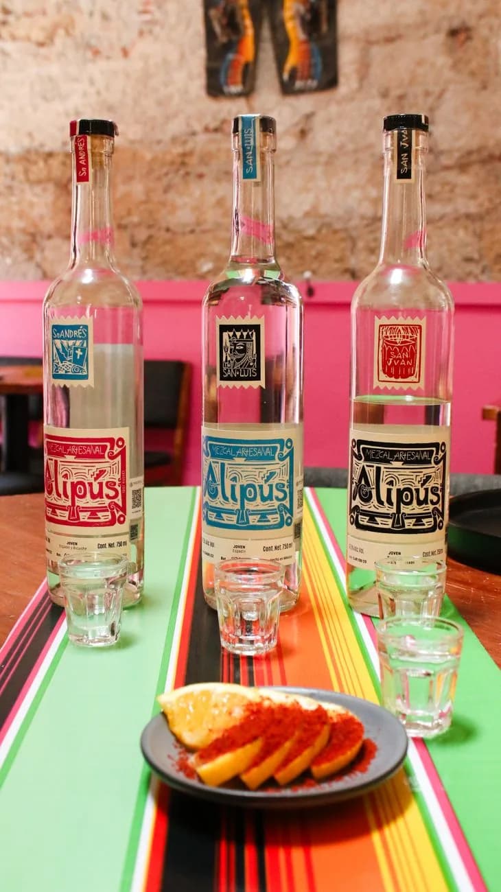 Bouteilles de mezcal artisanal et orange saupoudrée de piment sur une nappe serape dans une cantina mexicaine
