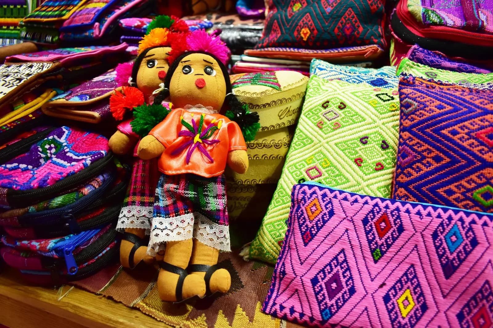 Coussins en textile brodé aux motifs géométriques et poupées artisanales sur un étal du marché de San Cristóbal de las Casas, au Chiapas