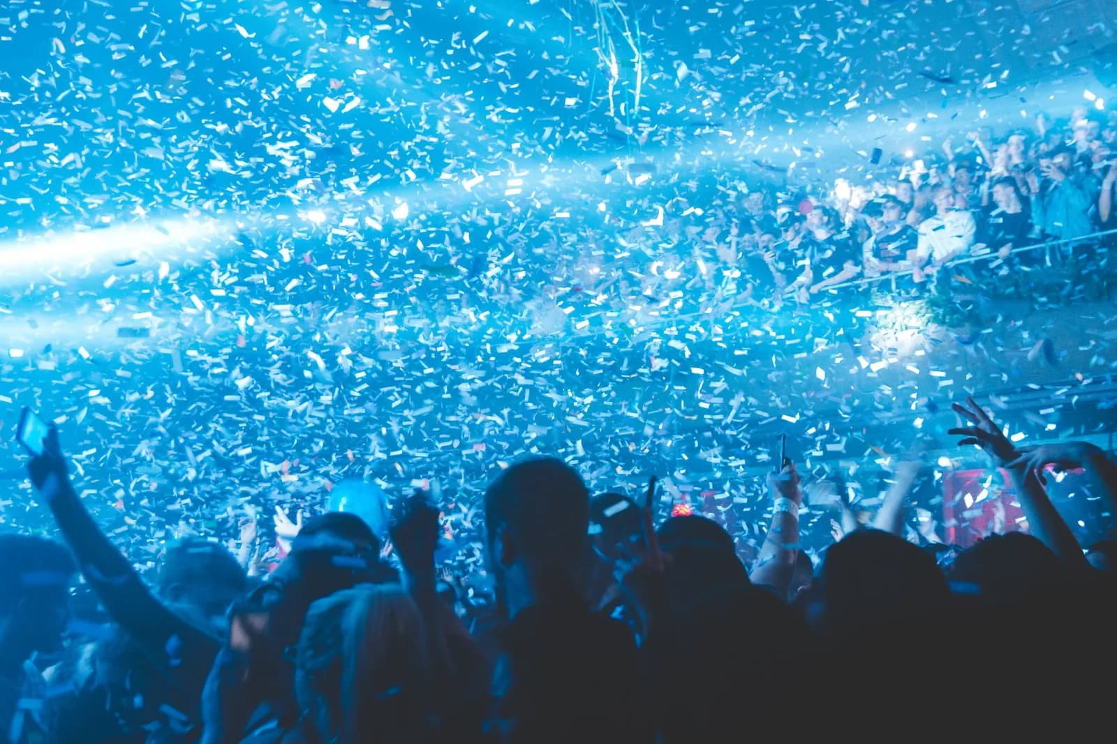 Foule vue de dos sous une pluie de confettis et de lumières bleues dans un club