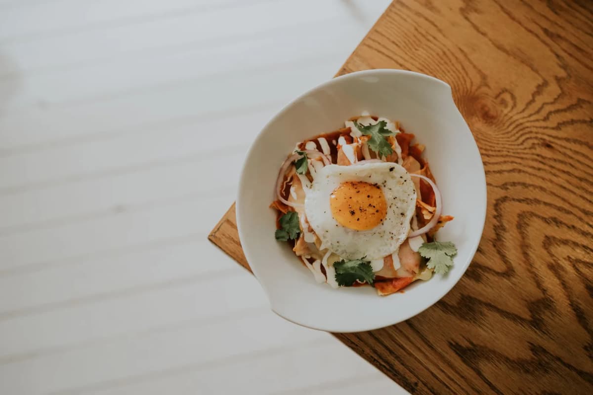 Bol de chilaquiles rouges mexicains avec œuf au plat, crème et oignon rouge