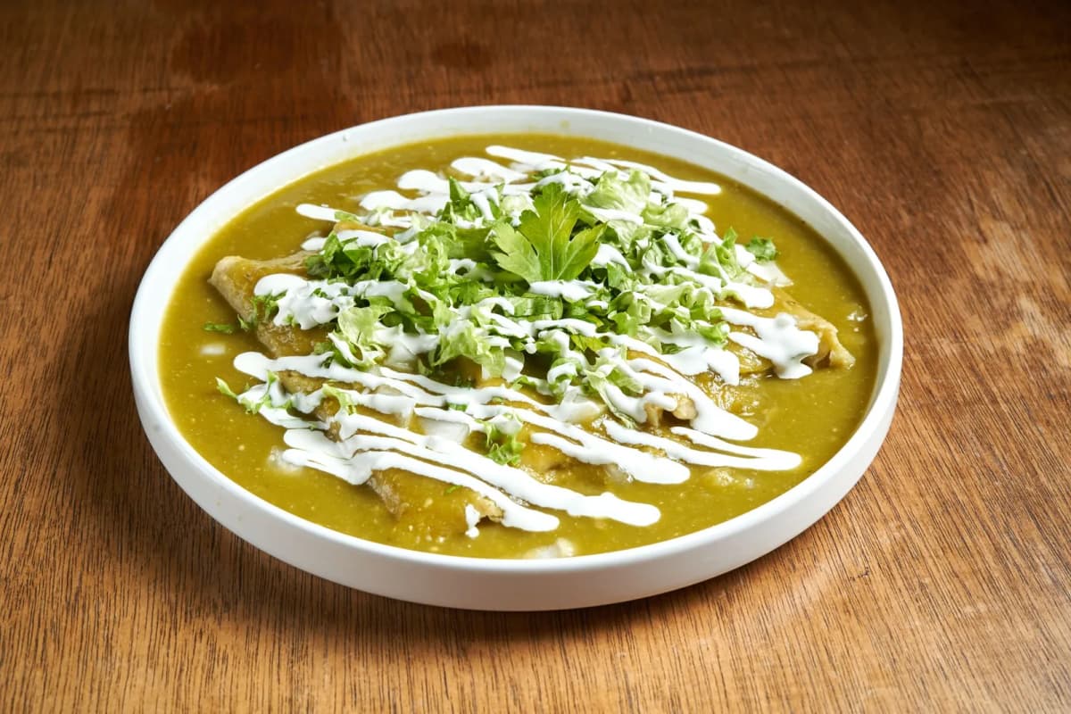 Assiette d'enchiladas verdes mexicaines nappées de crème et de laitue ciselée