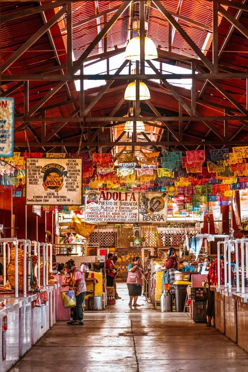 Allée d'un marché couvert traditionnel à Oaxaca au Mexique, avec ses étals de barbacoa et son papel picado coloré