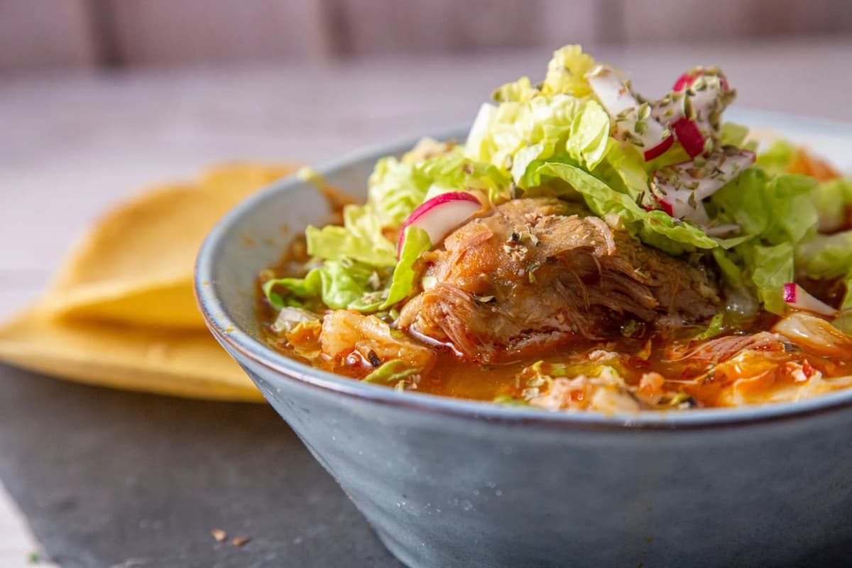 Bol de pozole rojo mexicain garni de laitue, radis et origan, avec des tostadas