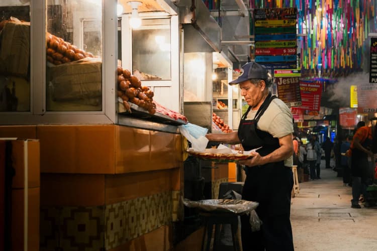 Vendeur de carnes asadas dans une allée de marché couvert à Oaxaca au Mexique, sous le papel picado