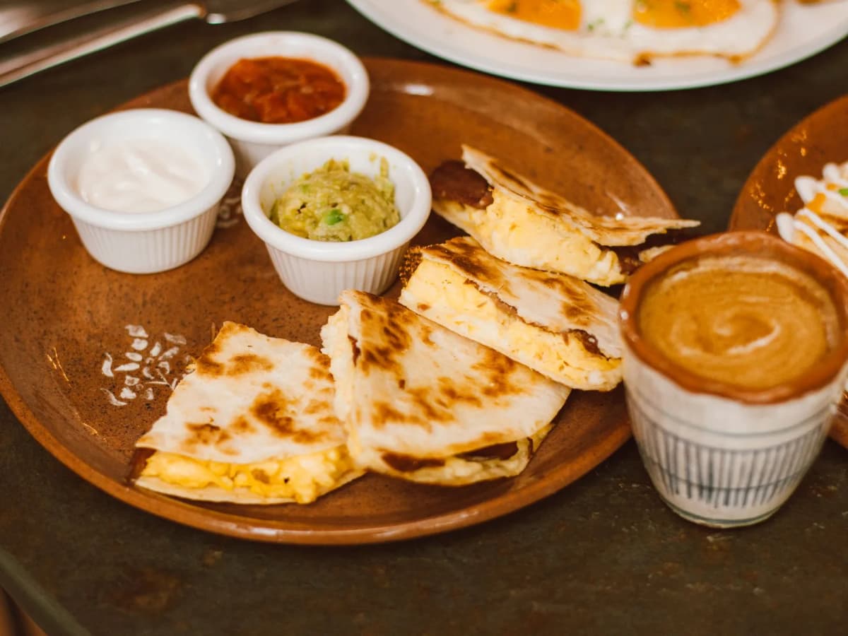 Quesadillas dorées coupées en parts dans une assiette de barro, avec crème, guacamole et salsa