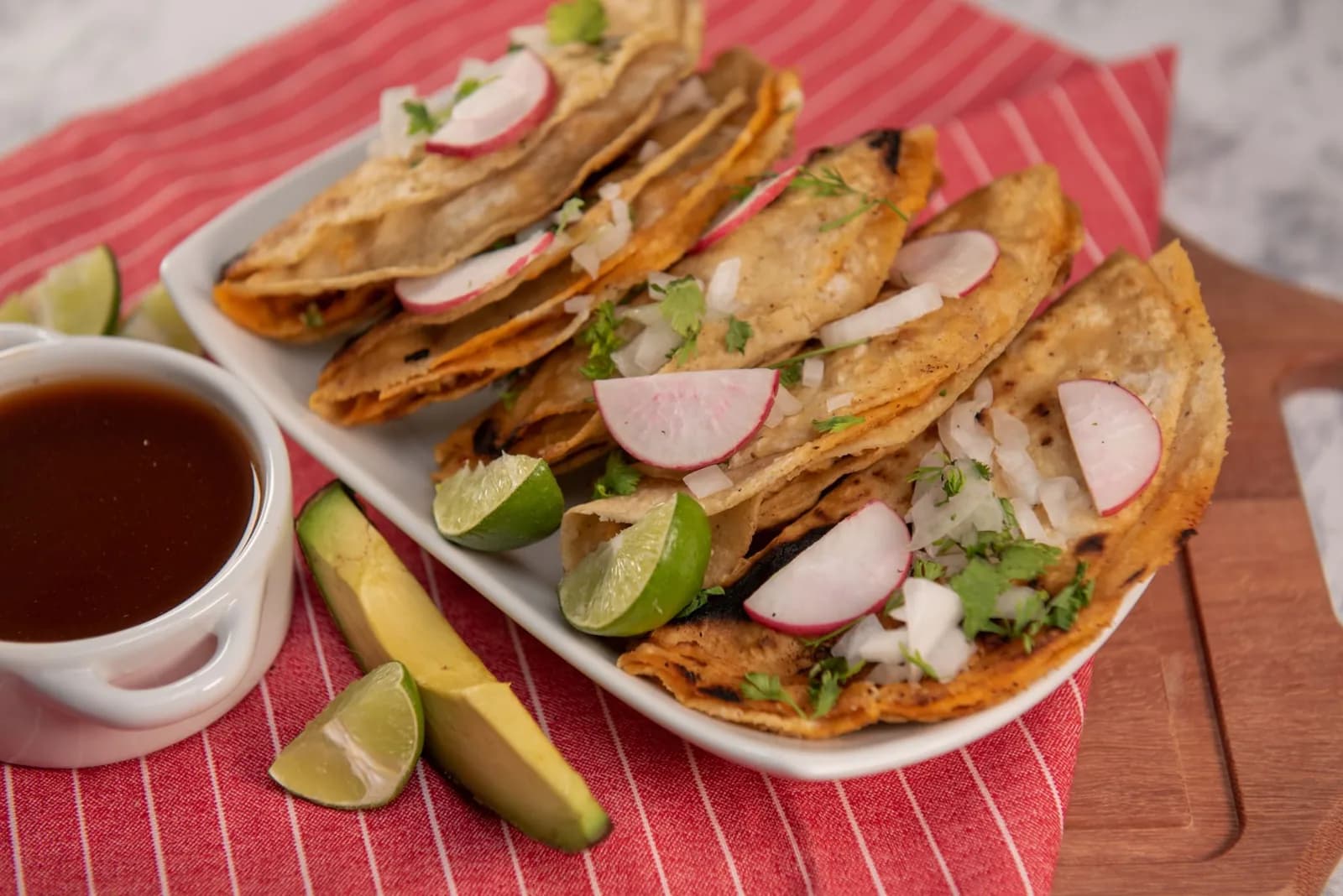Assiette de tacos dorados mexicains garnis de radis, oignon et coriandre, avec salsa et citron vert