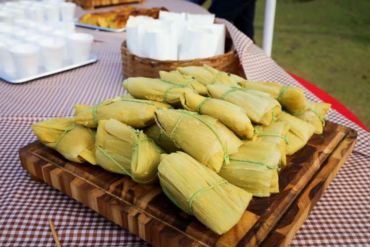 Tamales mexicains encore enveloppés dans leur feuille de maïs, empilés sur une planche