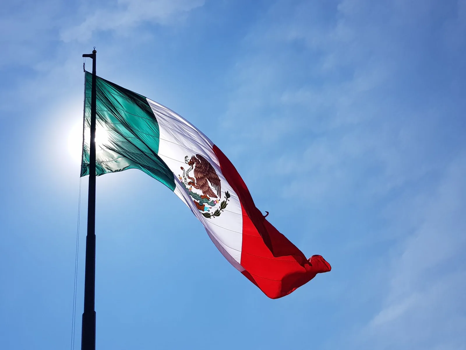 Drapeau du Mexique hissé sur sa hampe et déployé par le vent devant un ciel bleu