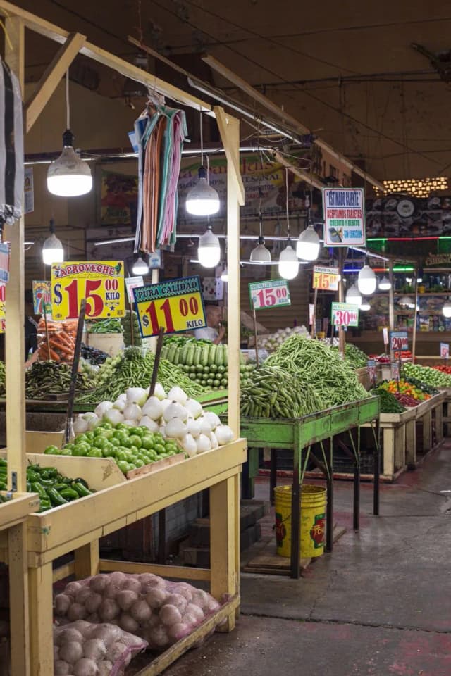 Étals de légumes et prix affichés en pesos sur un marché couvert au Mexique