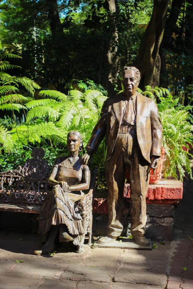 Statues en bronze de Frida Kahlo assise et de Diego Rivera debout, la main sur son épaule, dans un jardin de fougères à Mexico