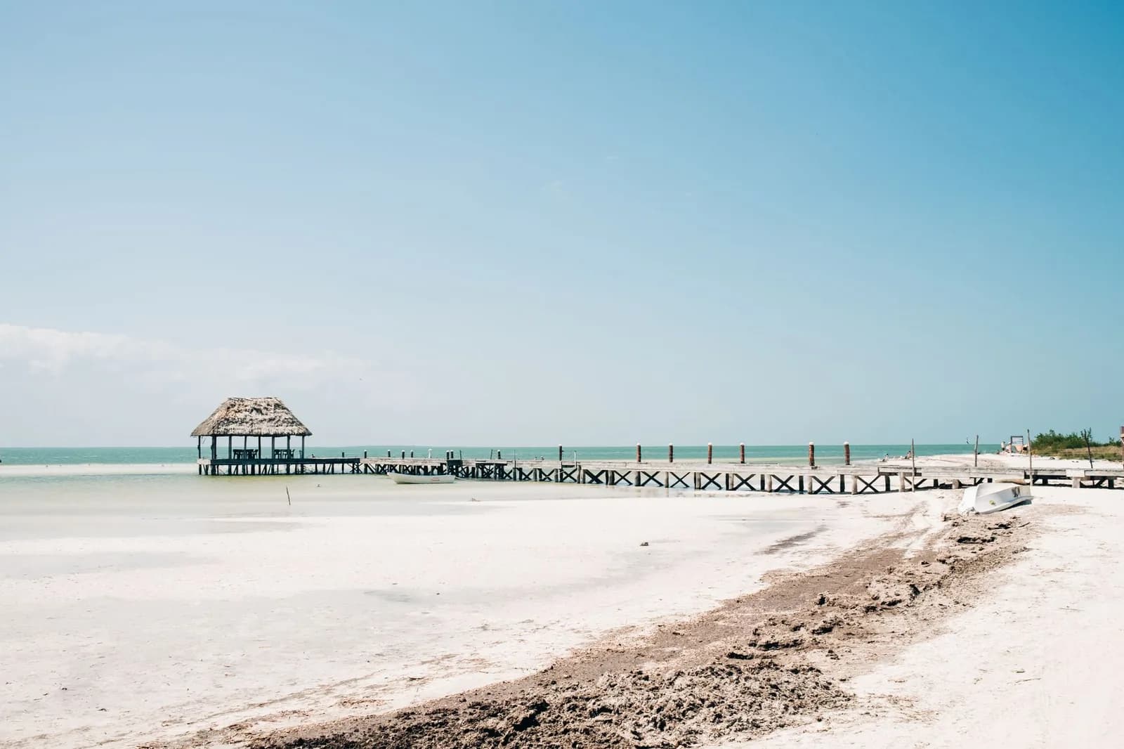 Plage de sable blanc d'Isla Holbox avec un ponton de bois et une palapa au bord d'une eau turquoise peu profonde