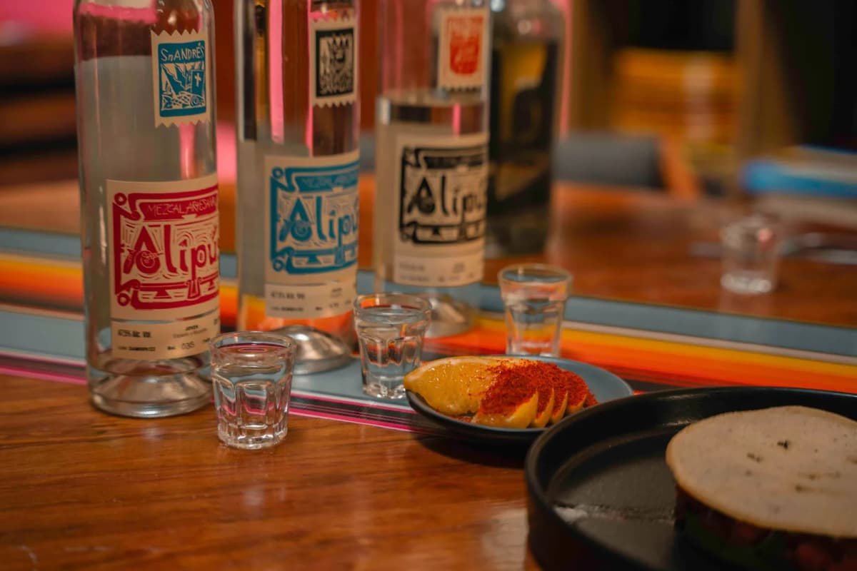 Verres de mezcal et tranches d'orange saupoudrées de sel rouge orangé, bouteilles en arrière-plan