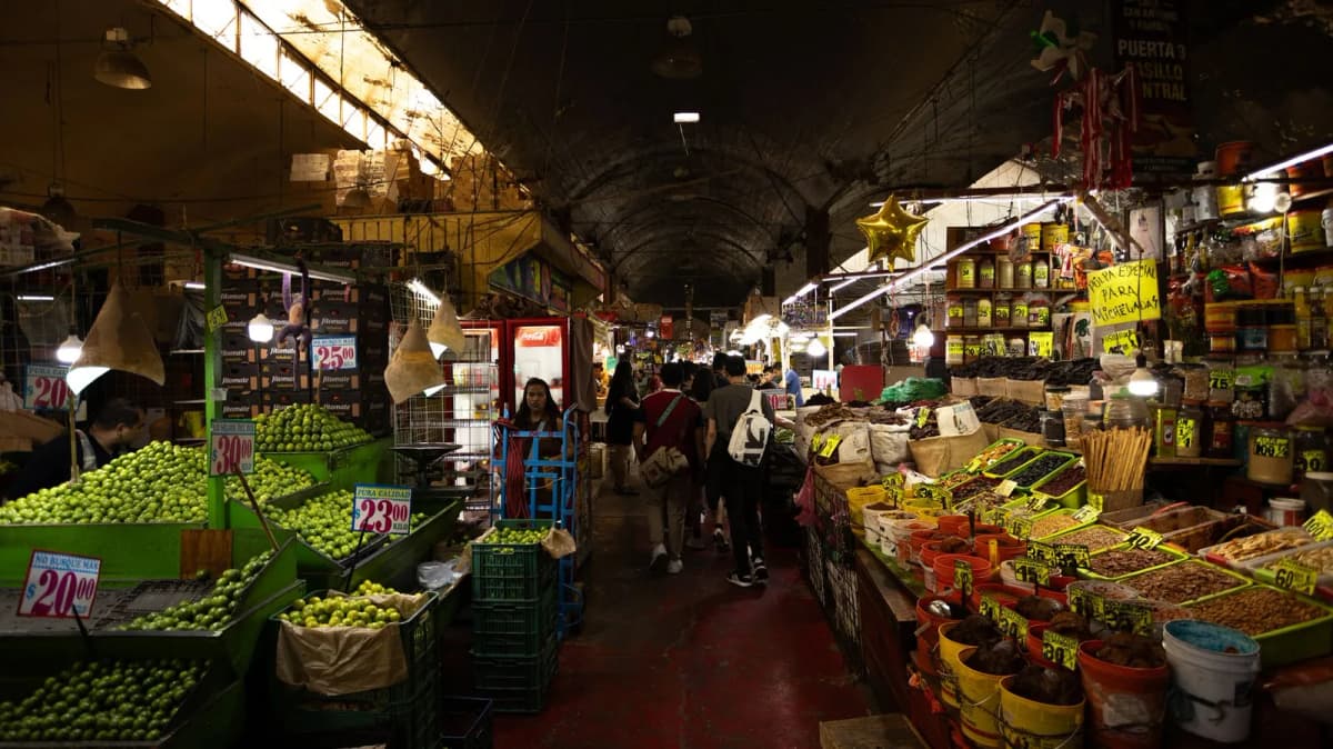Allée d'un marché couvert de Mexico, étals de fruits et légumes avec prix en pesos