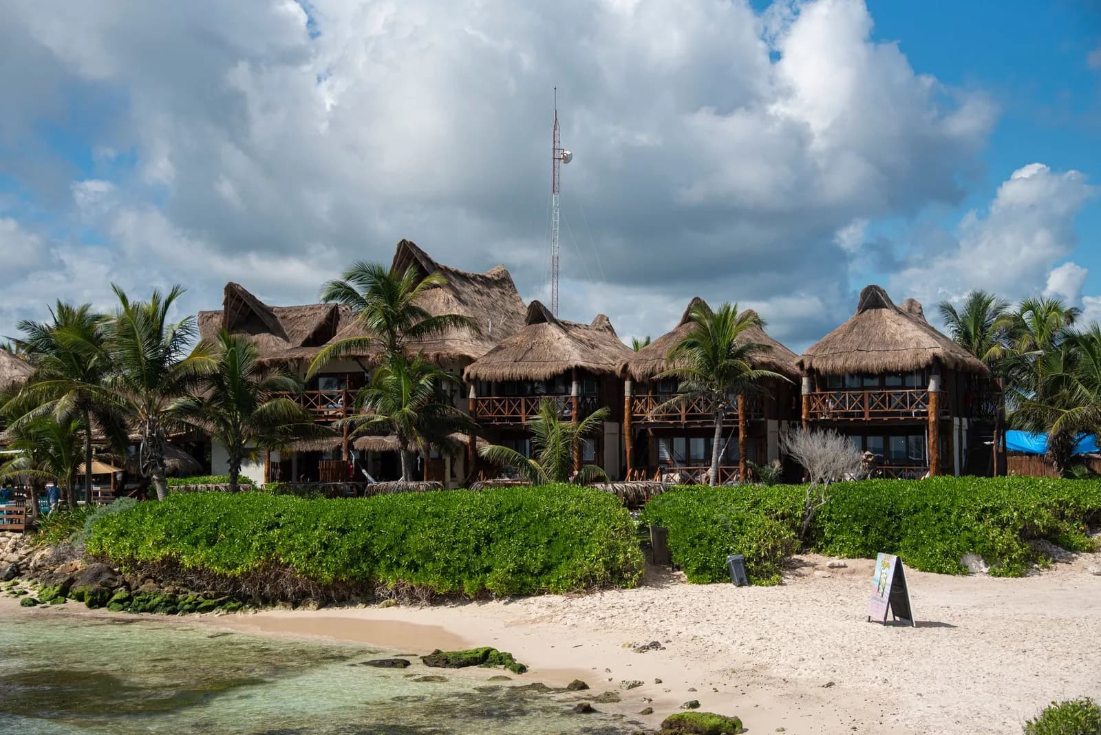 Hôtel en bois aux toits de palapa derrière la végétation, au bord d'une plage de sable blanc de la zone hôtelière de Tulum