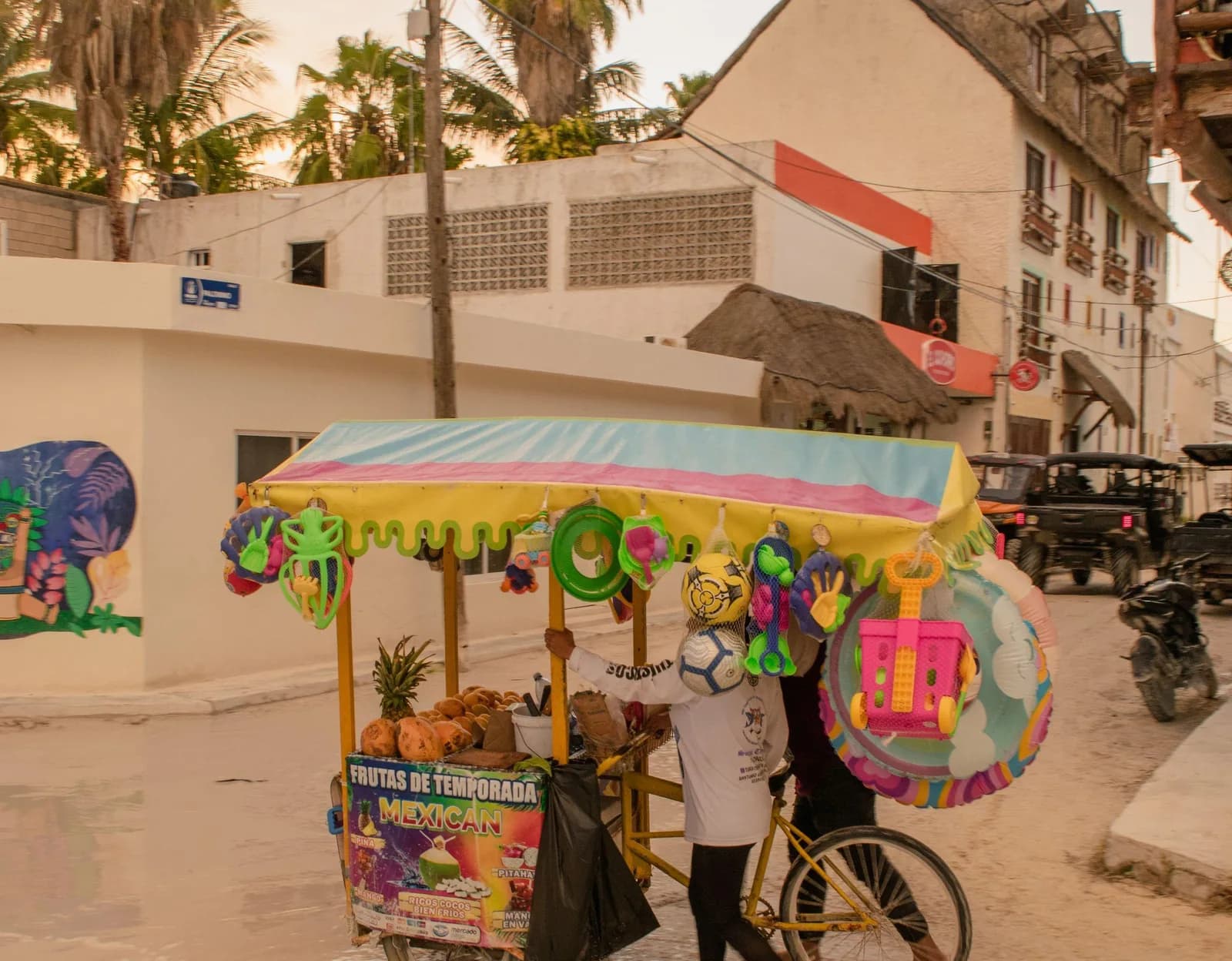 Charrette de fruits et jouets de plage dans une rue du centre de Tulum, bâtiments colorés et fresque murale