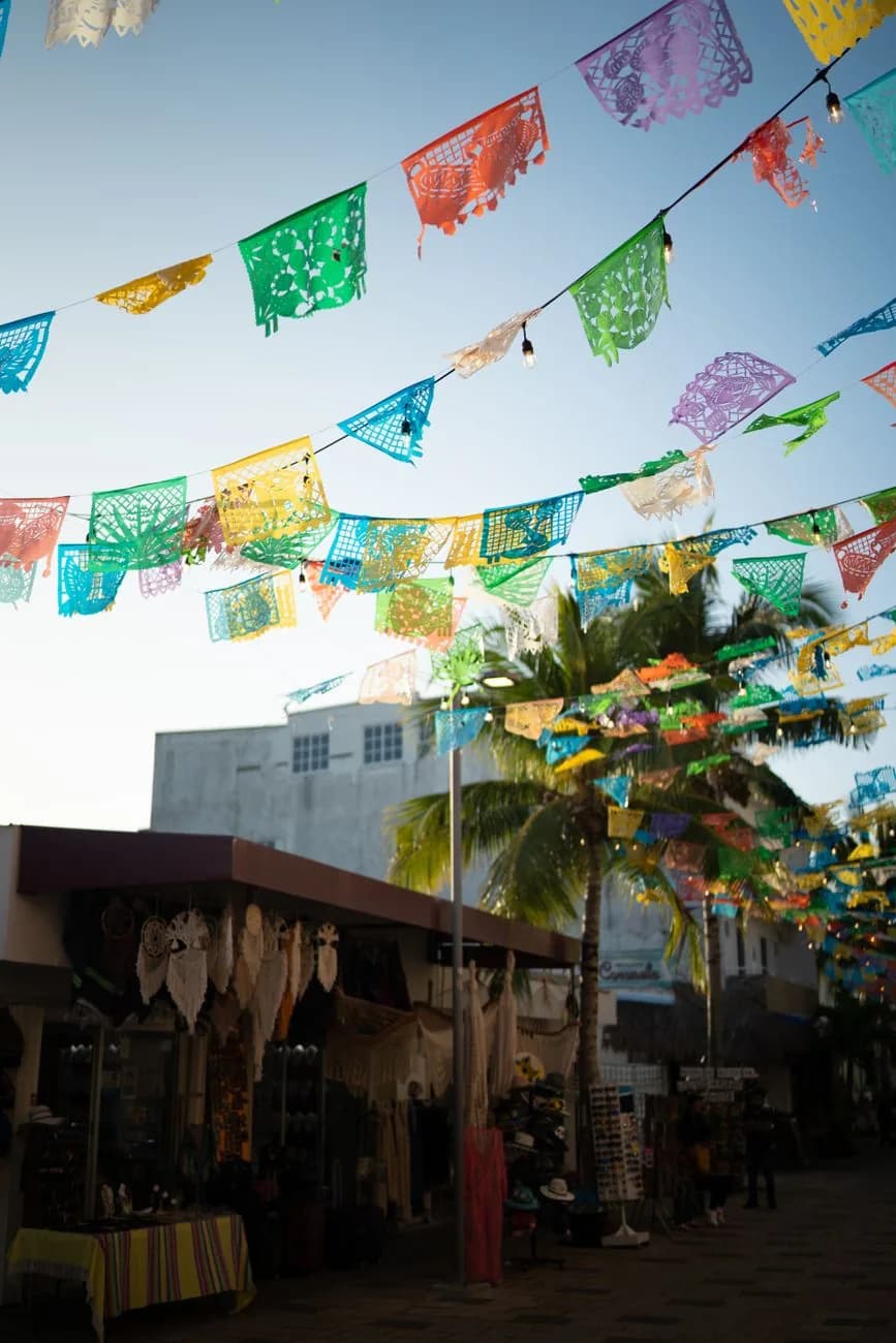 Rue commerçante de Playa del Carmen décorée de guirlandes de papel picado colorées, avec échoppes d'artisanat et palmiers