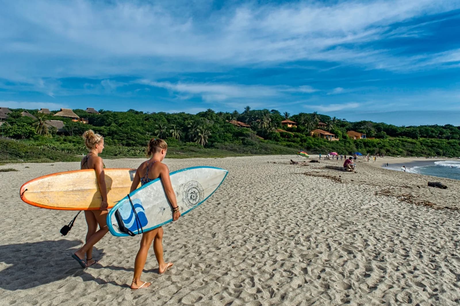 Deux surfeuses portant leur planche sur une large plage de sable