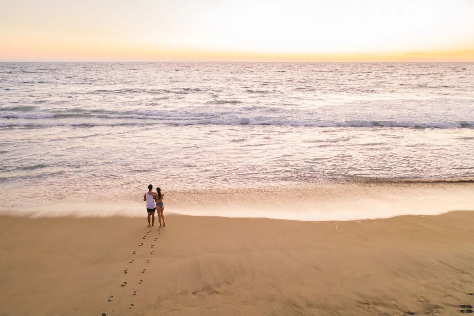 Longue plage de sable au crépuscule, avec des rouleaux et un couple sur le sable
