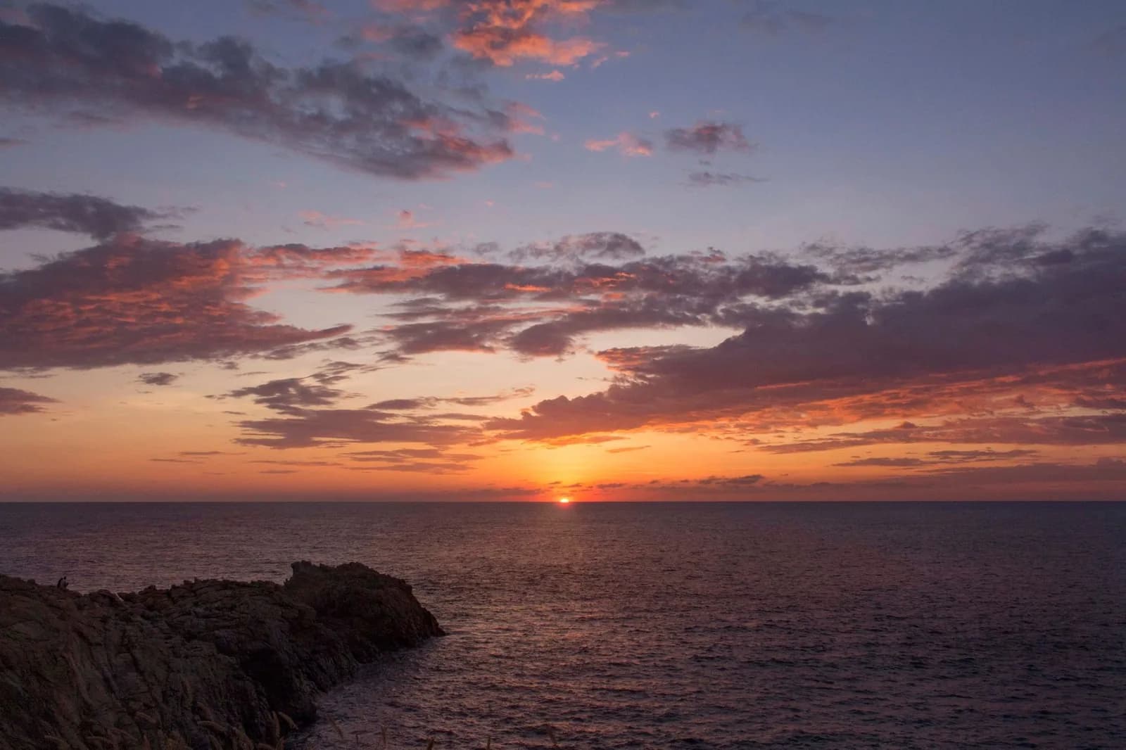Coucher de soleil sur l'océan Pacifique, avec un promontoire rocheux au premier plan