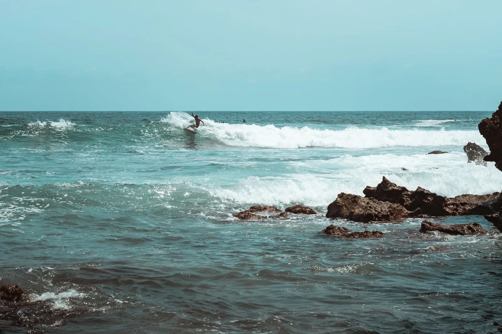 Surfeur sur une vague qui déferle près des rochers, sur la côte pacifique d'Oaxaca