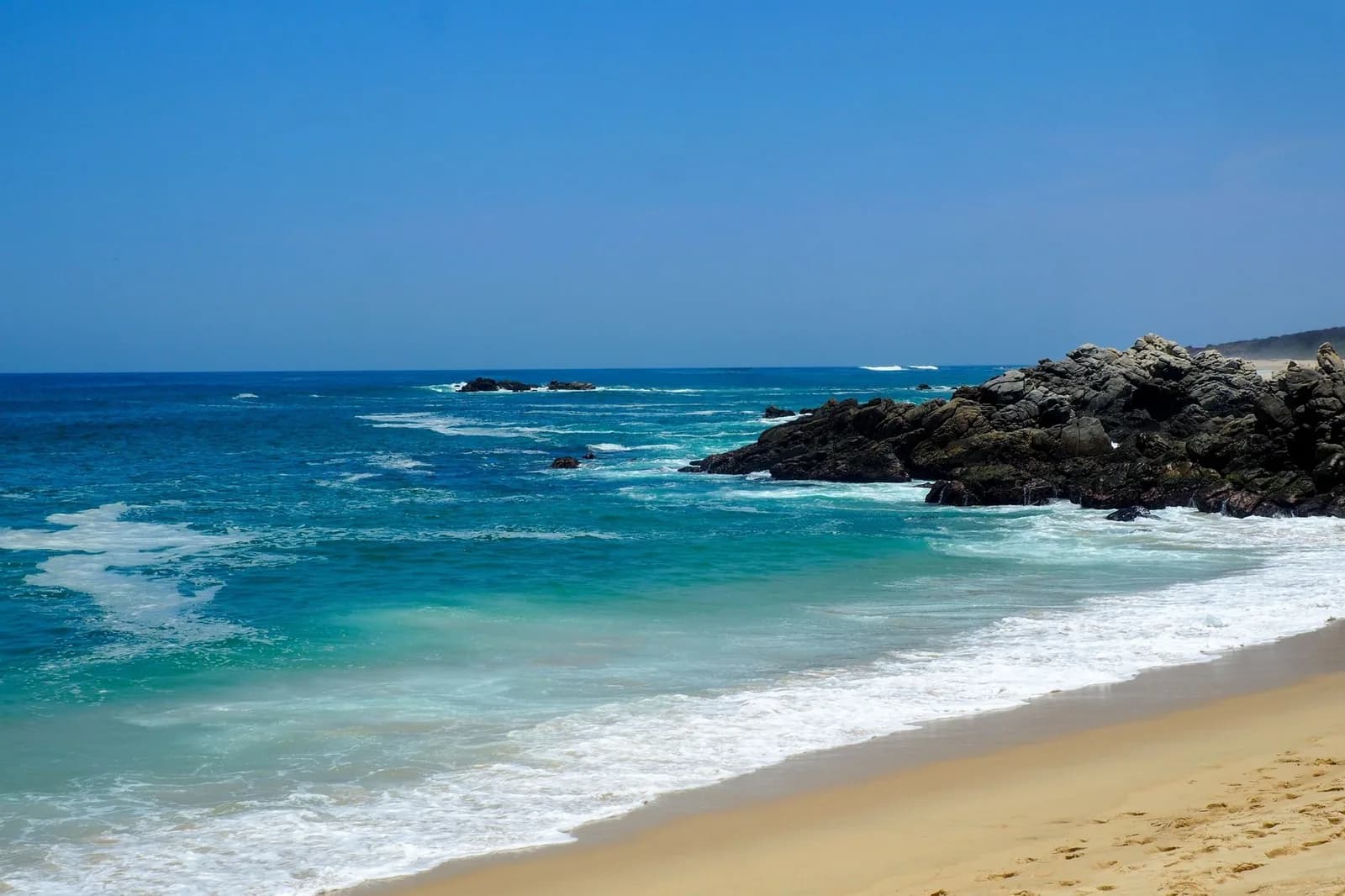Plage de sable avec des vagues turquoise et des rochers sombres, côte pacifique d'Oaxaca