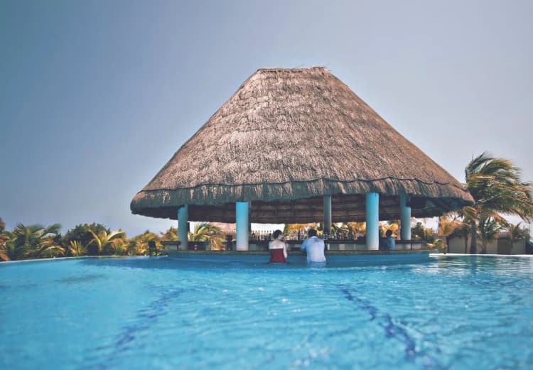 Bar de piscine sous un toit de palapa dans un resort tout inclus, avec des clients assis dans l'eau