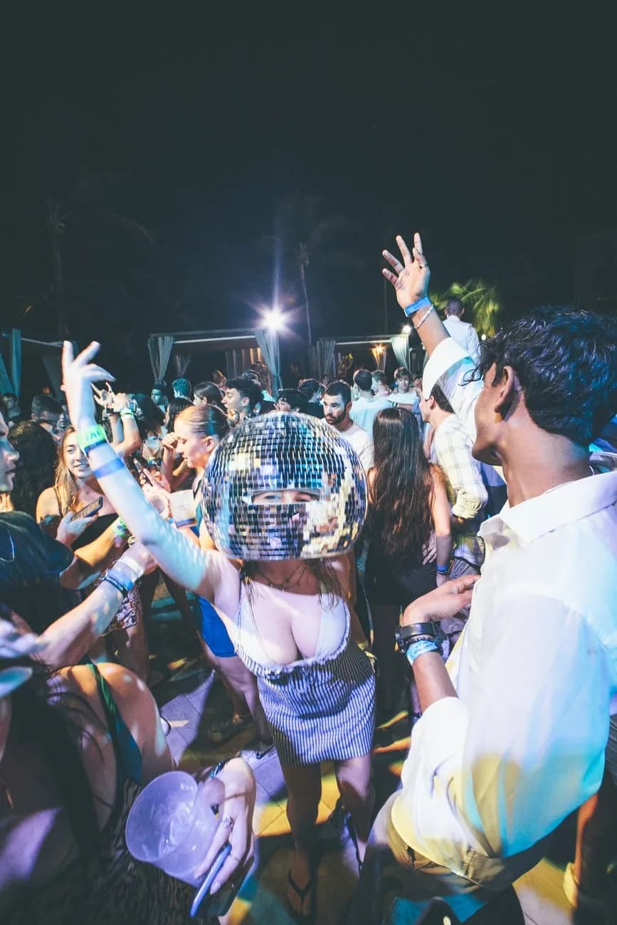 Foule dansant lors d'une fête de plage nocturne sous les palmiers, ambiance typique des soirées de Cancún