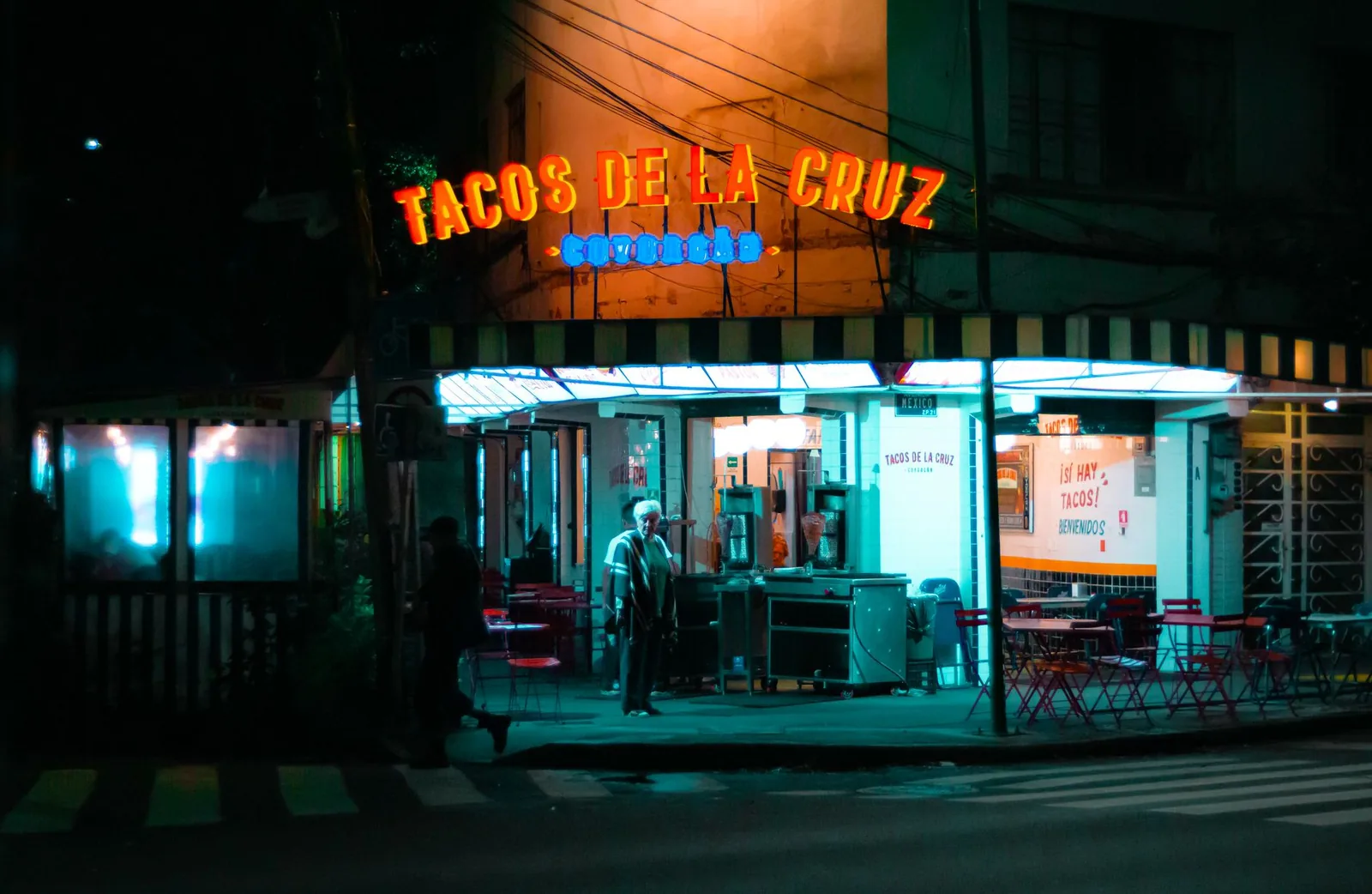 Taqueria mexicaine éclairée au néon la nuit, avec terrasse sur le trottoir