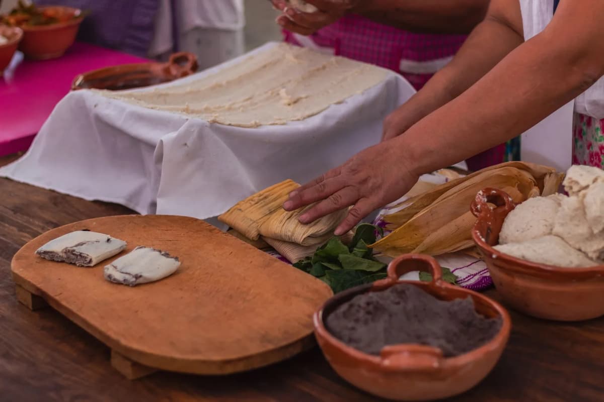 Mains qui étalent la pâte de maïs sur une feuille de maïs, avec des bols de masa et de purée de haricots noirs pour préparer des tamales