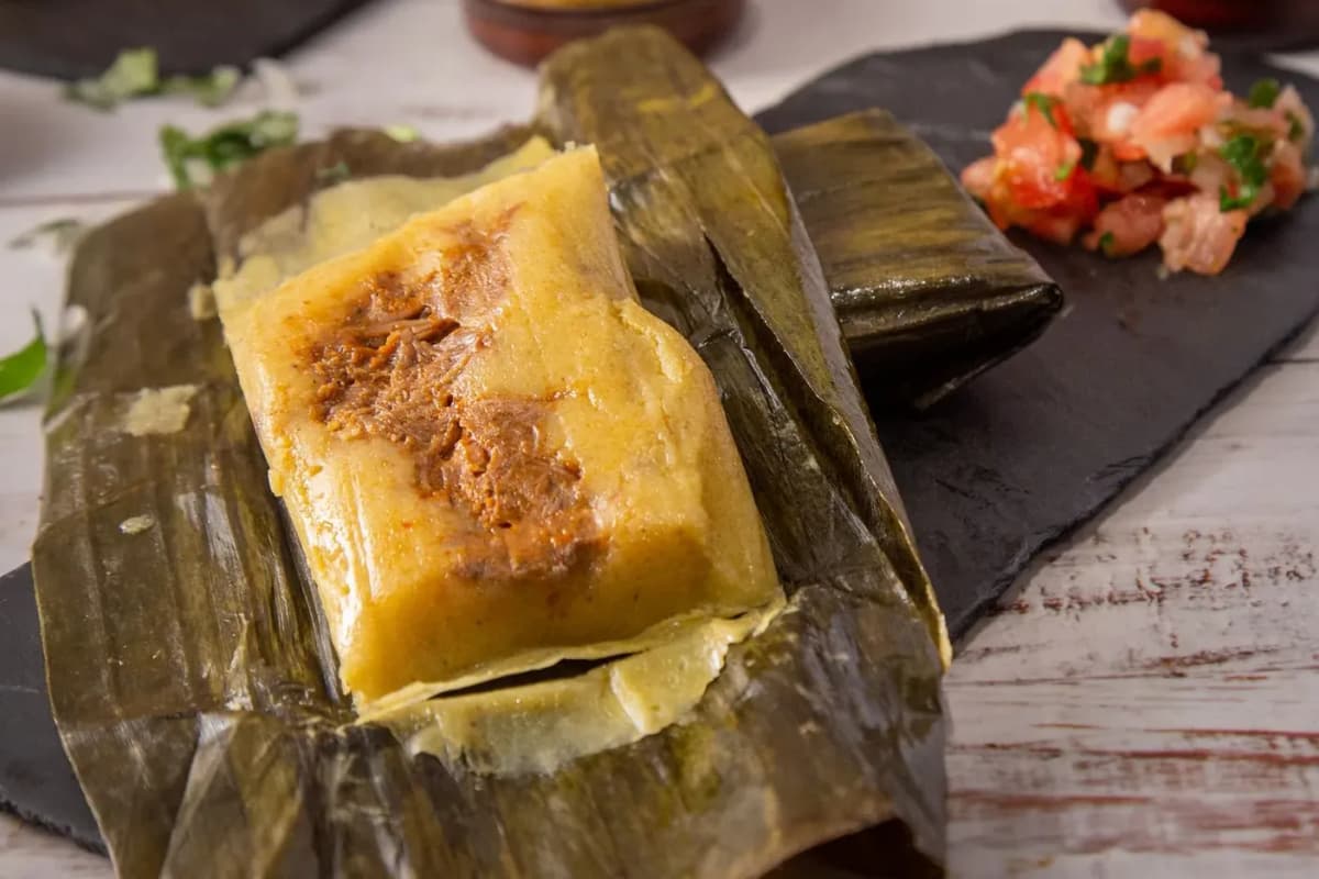 Tamal à la viande effilochée en sauce rouge, ouvert dans sa feuille de bananier, avec de la salsa fraîche