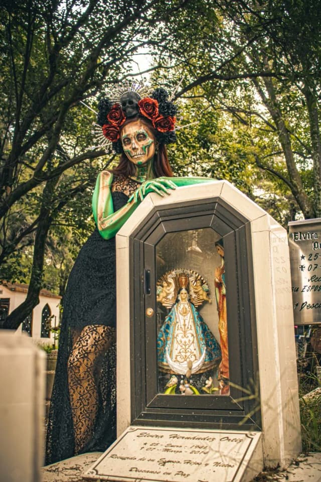 Femme costumée en Catrina au maquillage de calavera, couronne de roses noires et rouges, dans un cimetière mexicain